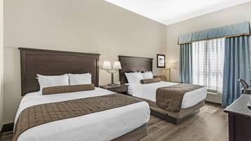 A hotel room with two beds, a desk, and a window with curtains.
