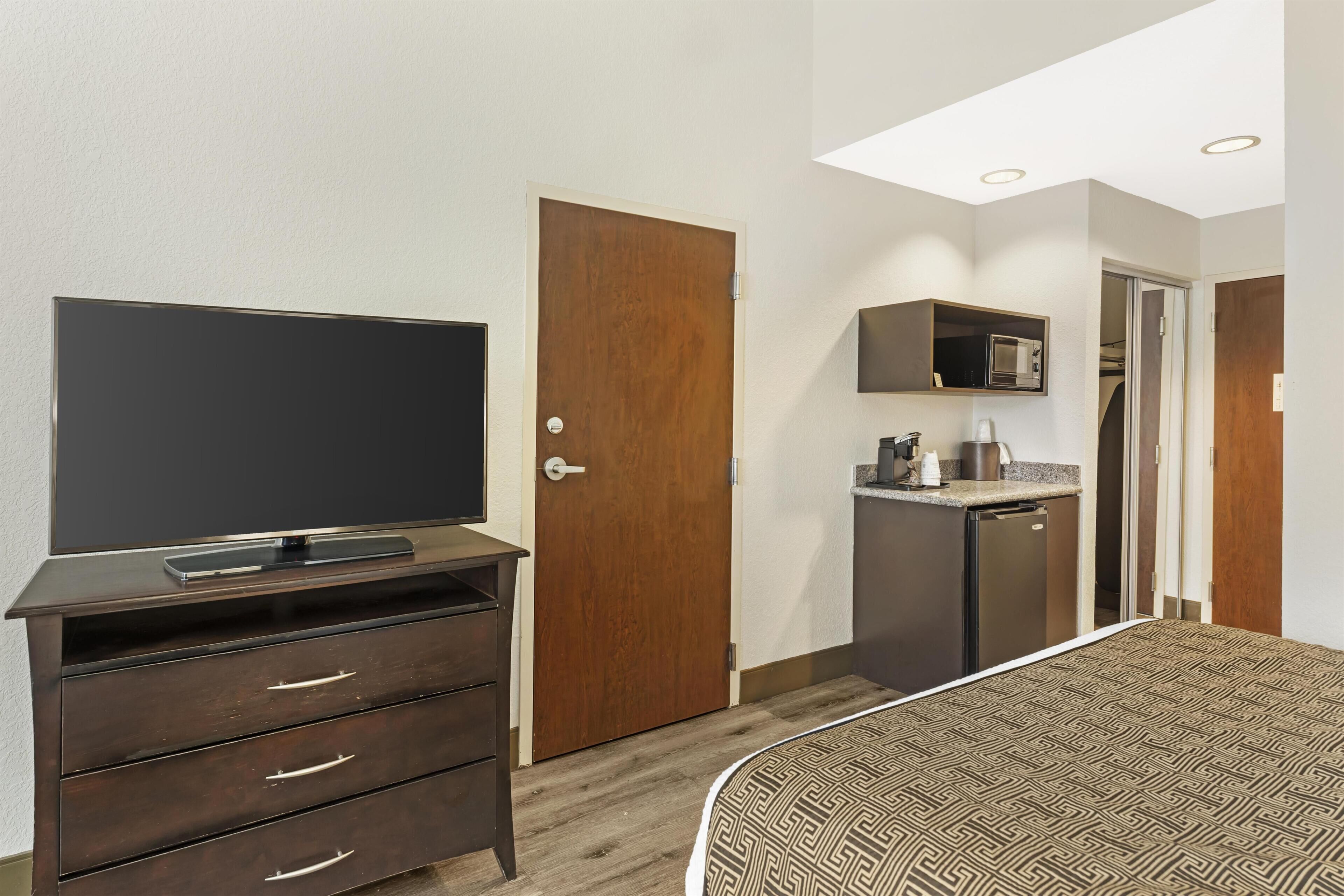 A hotel room with a bed, a TV on a dresser, a microwave, and a small kitchenette.