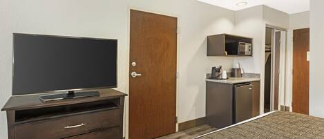 A hotel room with a bed, a TV on a dresser, a microwave, and a small kitchenette.
