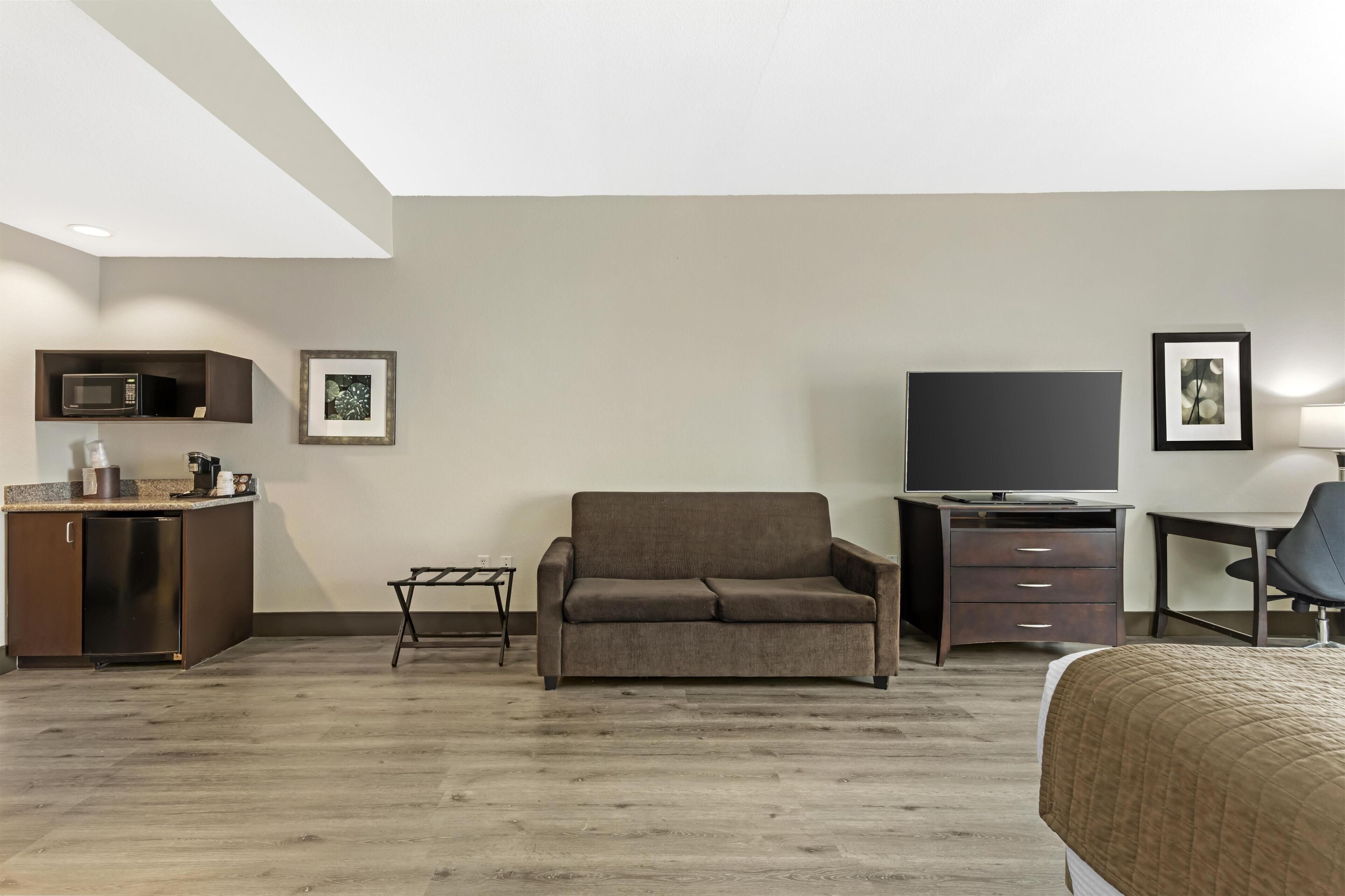 Una habitación de hotel moderna con kitchenette, sofá, televisor, escritorio y cama.