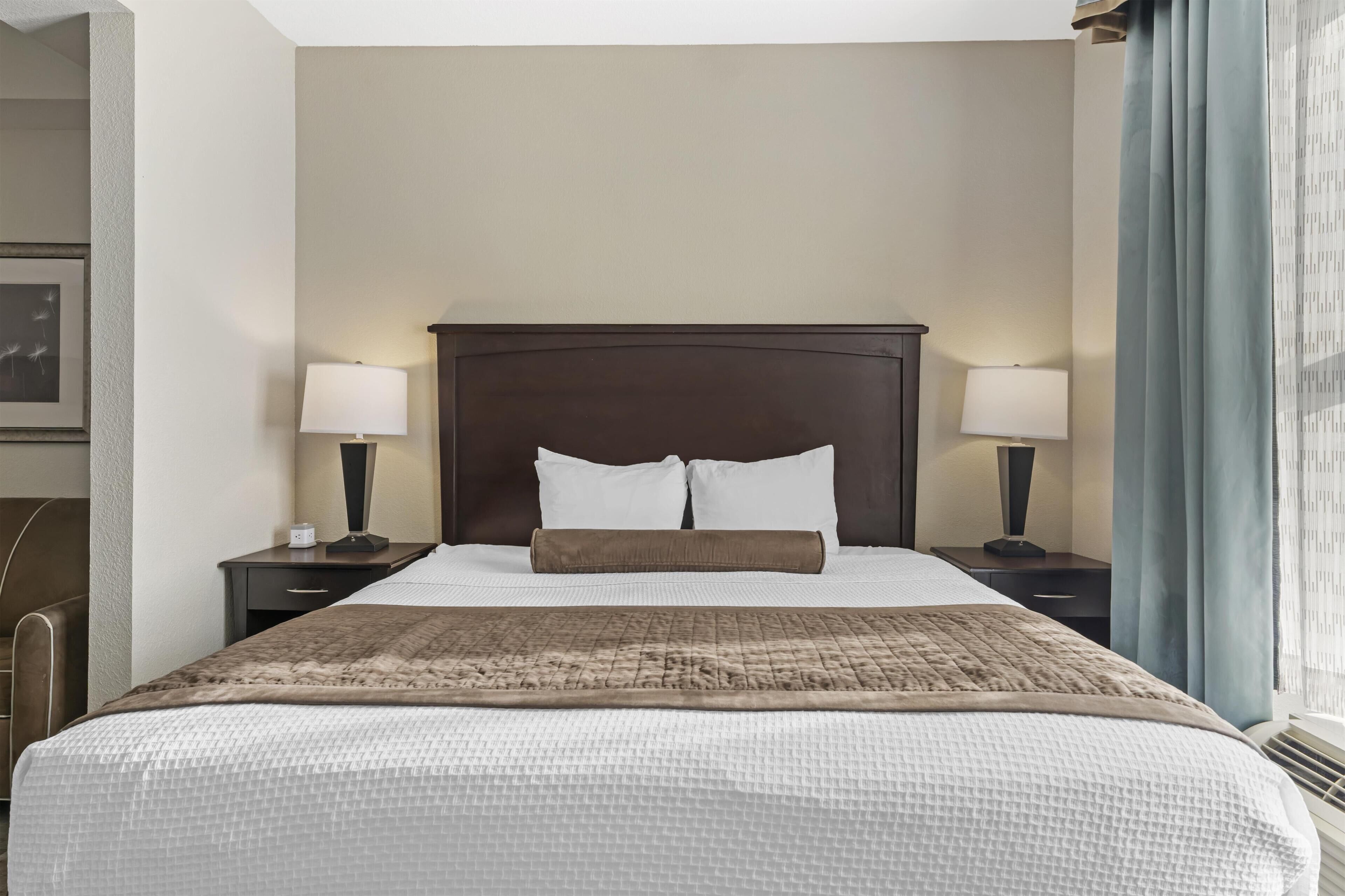 A neatly made bed with a headboard, two bedside tables with lamps, and a window with curtains.