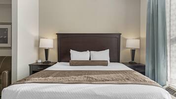 Una cama bien hecha con cabecera, dos mesitas de noche con lámparas y una ventana con cortinas.