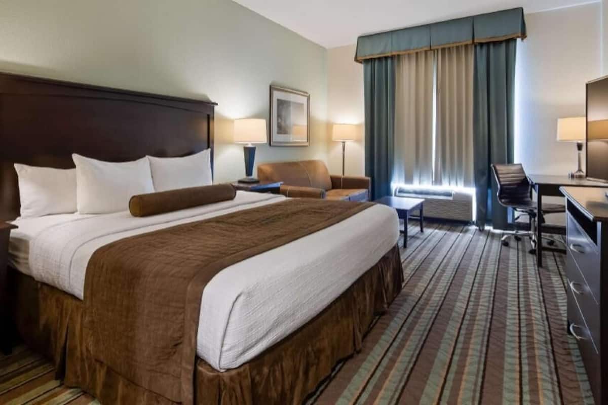 Une chambre d’hôtel avec un grand lit, un bureau, une chaise, une télévision et une fenêtre avec des rideaux.