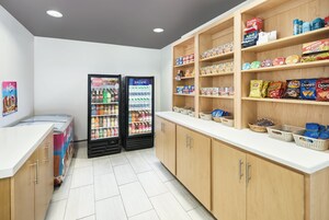 Un área limpia y bien organizada para snacks y bebidas, con dos dispensadores, estantes llenos de refrigerios y una encimera blanca.