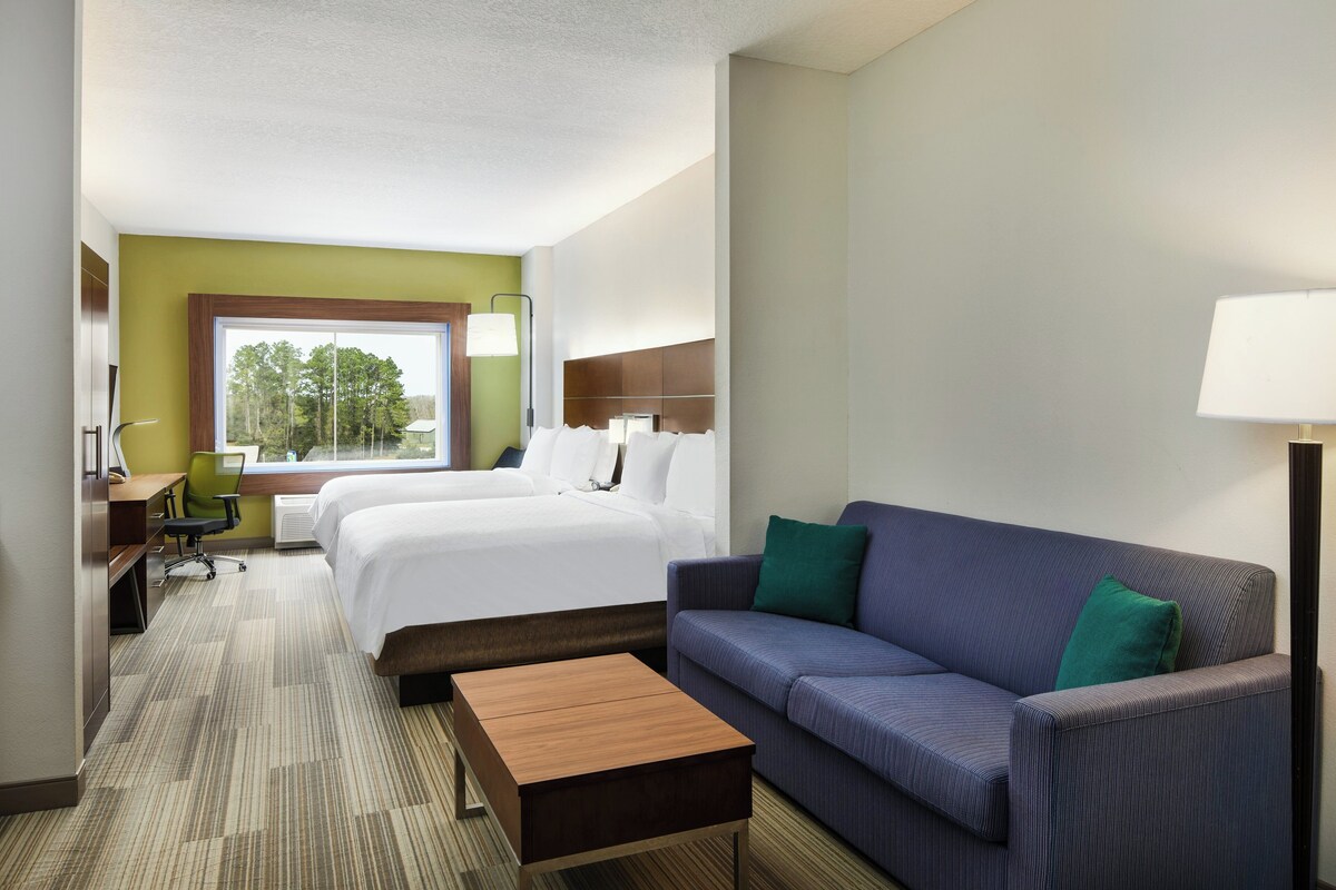 A hotel room with a bed, a sofa, a desk, and a window with a view of trees.
