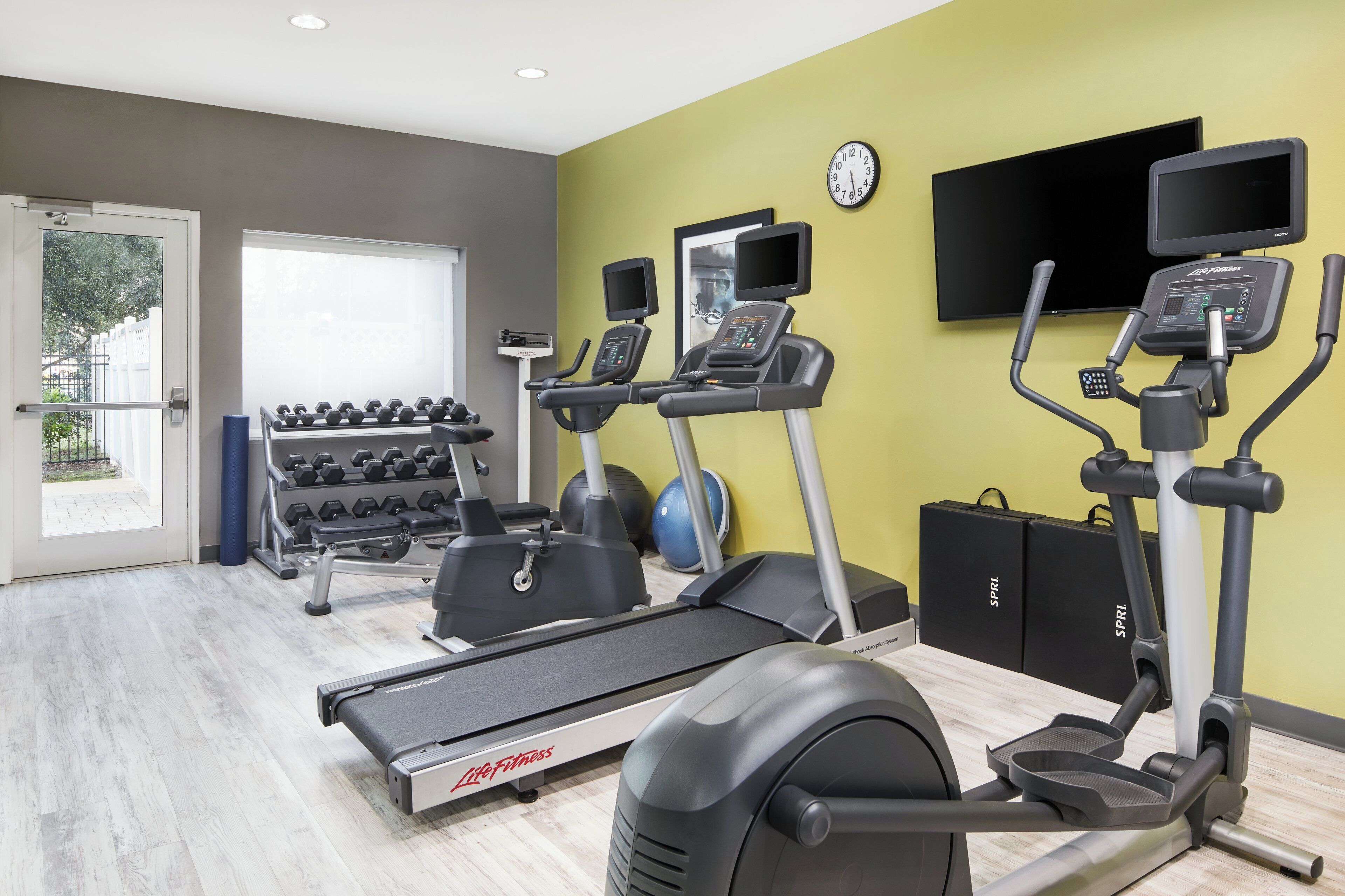 A gym with treadmills, elliptical machines, and dumbbells.