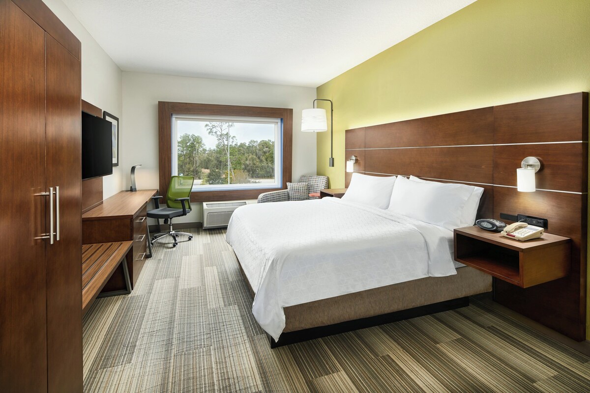 A hotel room with a bed, desk, chair, and a television.