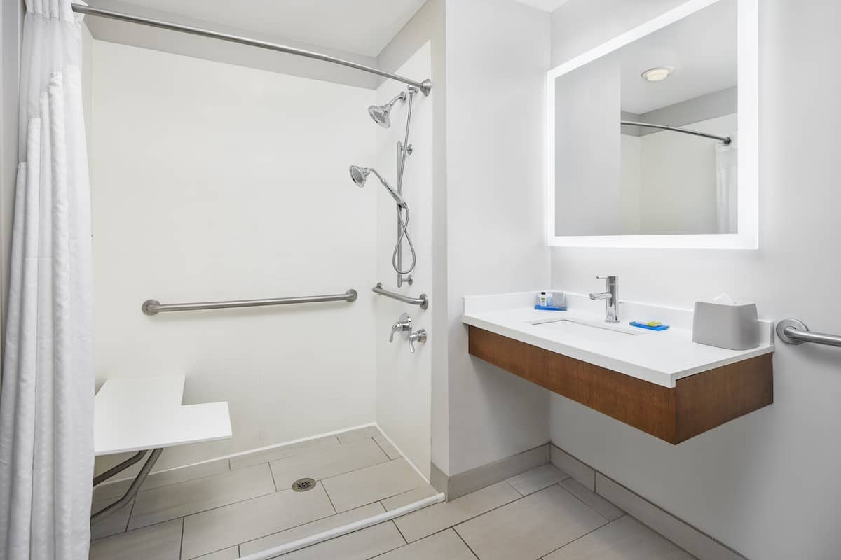 A modern bathroom with a shower, grab bars, a sink with a mirror, and a towel rack.