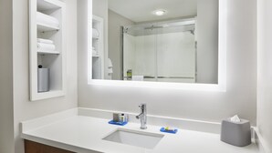 Ein modernes Badezimmer mit einem weißen Waschbecken, einem Spiegel und einer Duschkabine aus Glas.