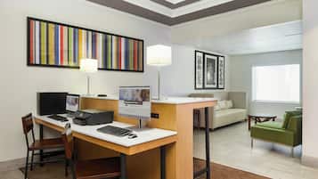 Habitación de hotel con escritorio, computadora, sillas, sofá, una mesita y obras de arte en las paredes.