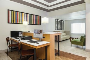 A hotel room with a desk, computer, chairs, a sofa, a small table, and artwork on the walls. - Holiday Inn Express Palatka Northwest by IHG (Palatka)