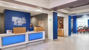 Zona de recepción de un hotel, con mostrador de recepción, una barra de atención y un área de estar con mesas y sillas.