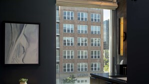A modern bathroom with a toilet, a small potted plant, a framed abstract artwork, and a view of a brick building through a window. - The Lloyd Stamford, Tapestry Collection by Hilton (Stamford)