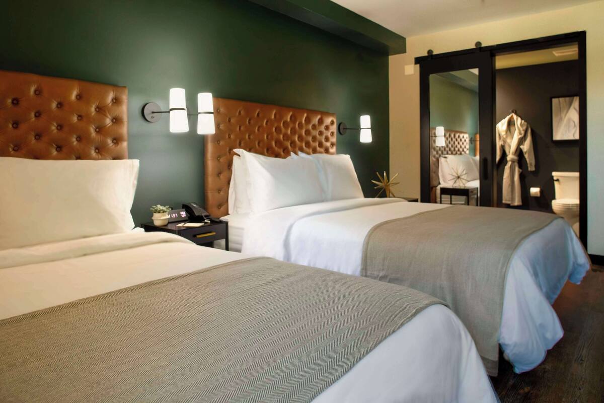 Une chambre d’hôtel avec deux lits, une tête de lit marron et un mur vert.