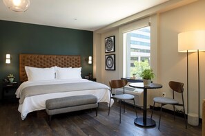 A hotel room with a large bed, a round table with chairs, a bench, and a window with a view of buildings. - The Lloyd Stamford, Tapestry Collection by Hilton (Stamford)