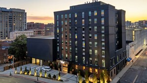 A modern hotel with a prominent corner location, featuring a large entrance, a parking lot, and a landscaped area with illuminated plants. - The Lloyd Stamford, Tapestry Collection by Hilton (Stamford)