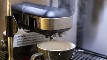 Una cafetera con vapor saliendo, una taza de metal y una etiqueta de advertencia.