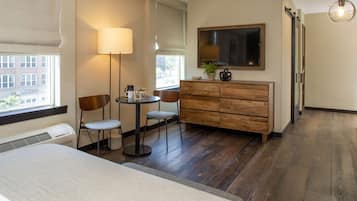 A hotel room with a bed, a desk with two chairs, a small table, a lamp, a TV, and a dresser.