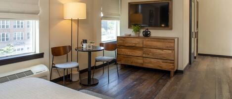 A hotel room with a bed, a desk with two chairs, a small table, a lamp, a TV, and a dresser.