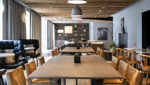 A modern dining area with a large wooden table, cushioned chairs, pendant lighting, and a bookshelf in the background. - The Lloyd Stamford, Tapestry Collection by Hilton (Stamford)