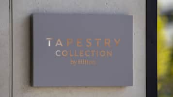 Un letrero con el texto 'TAPESTRY COLLECTION by Hilton' sujeto a una pared.