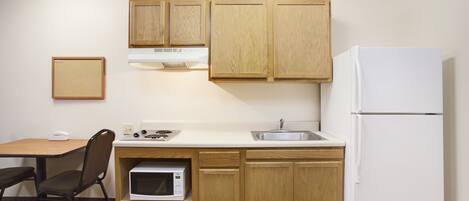 A compact kitchen with wooden cabinets, a white refrigerator, a microwave, and a sink.
