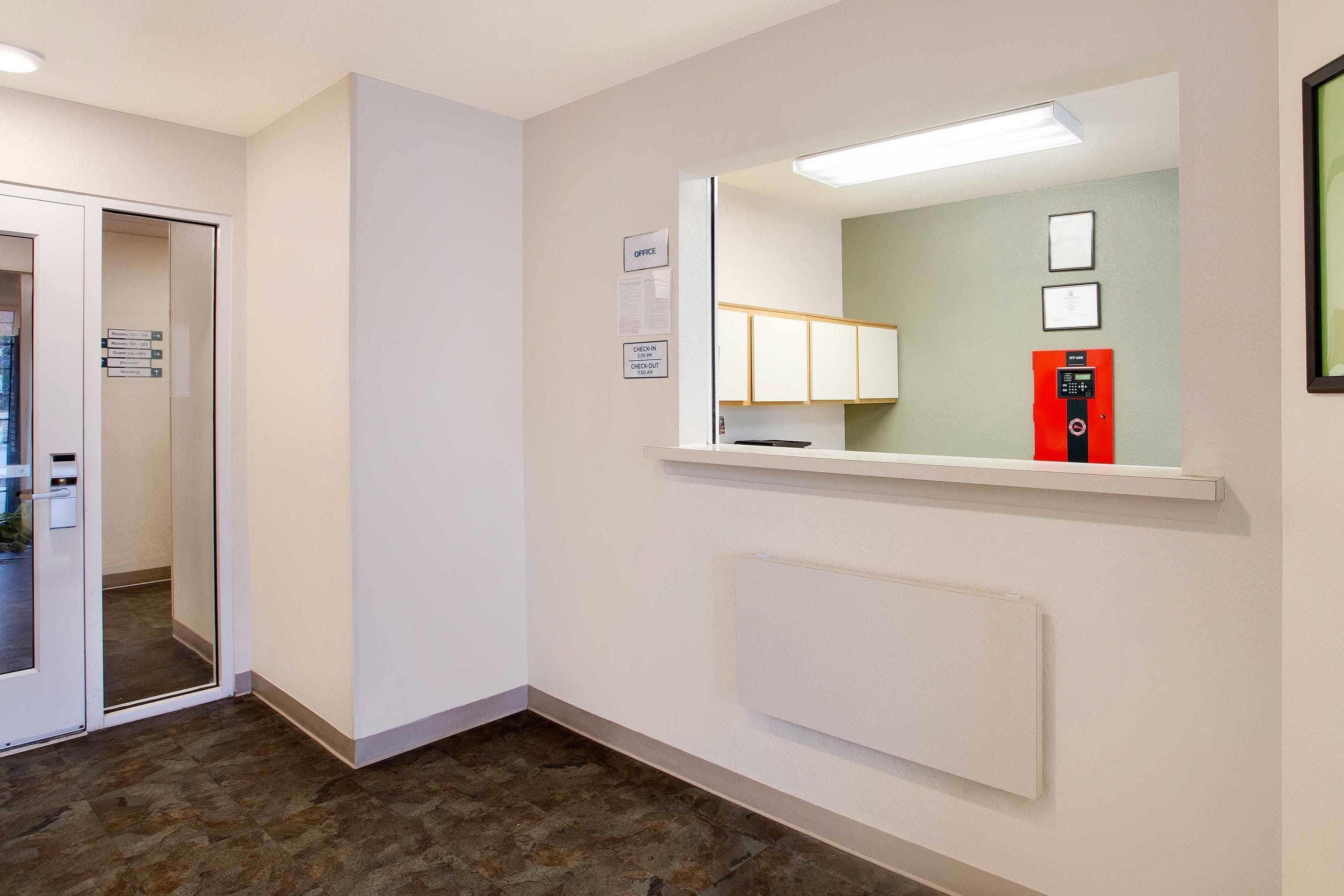 A hotel corridor with a check-in/check-out counter, a mirror reflecting a room, and a radiator on the wall.