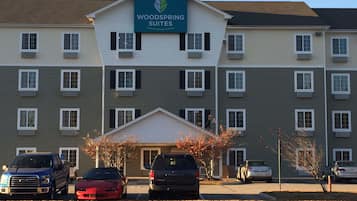 A multi-story hotel with a sign reading "Woodspring Suites." There are several cars parked in front, and the building has a symmetrical facade with evenly spaced windows.