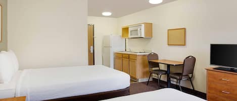 A hotel room with two beds, a desk with a chair, a microwave, a television, and a small cabinet.