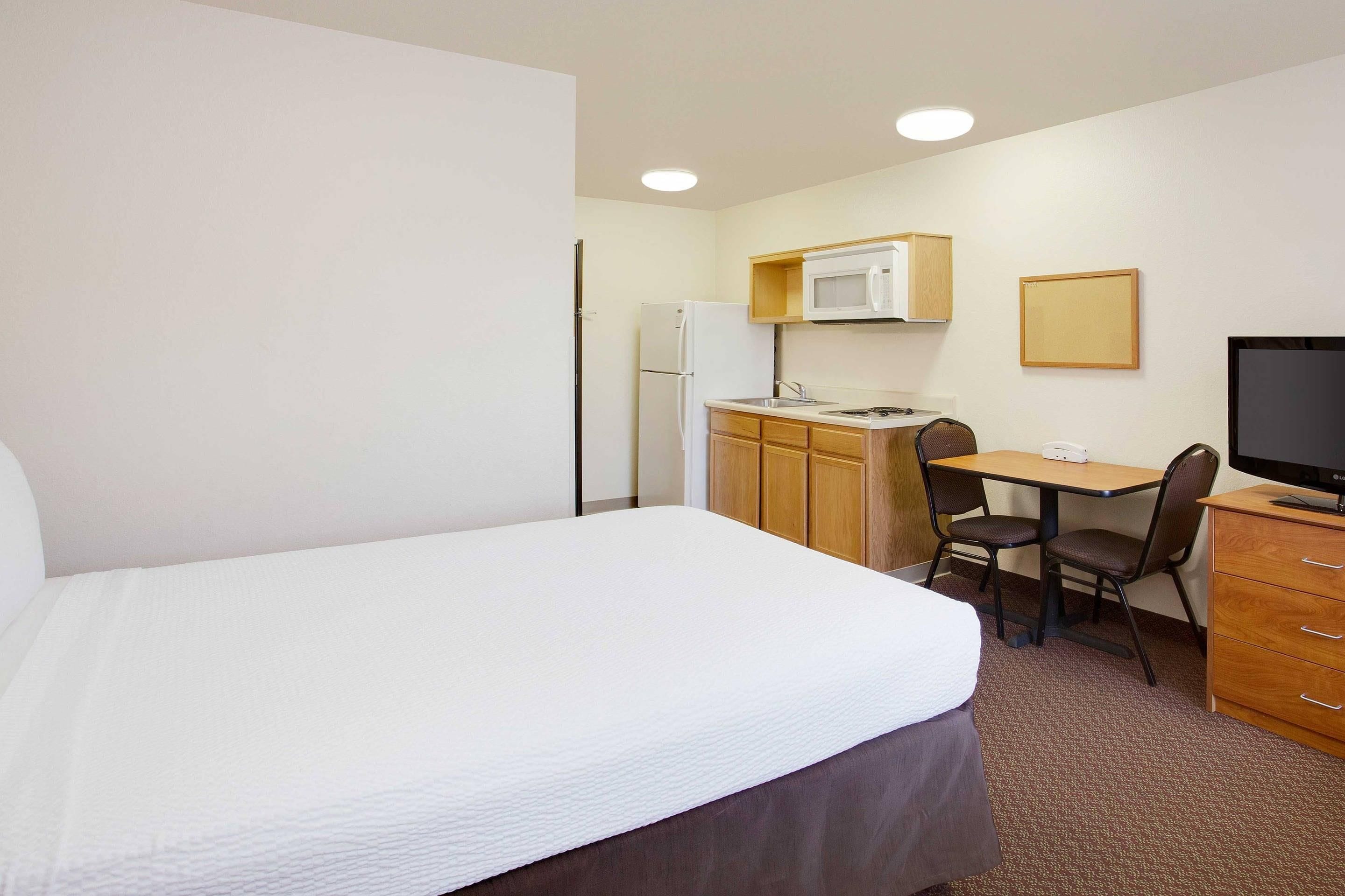 A hotel room with a bed, a desk, a chair, a television, a microwave, and a refrigerator.