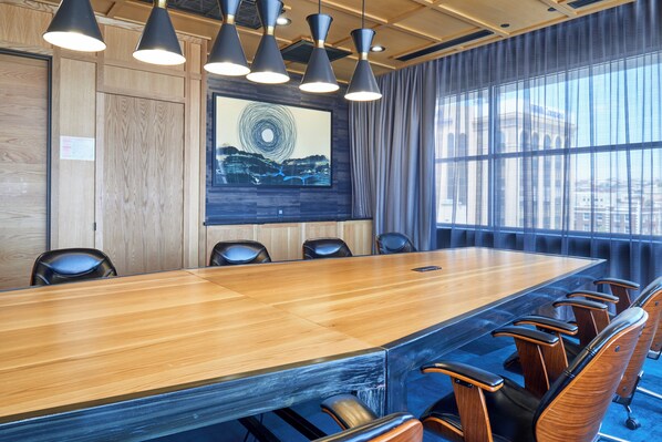 A conference room with a long table, six chairs, and a large window with curtains.