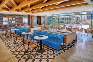 A modern interior with a mix of seating options including benches and tables, a patterned floor, and a view through large windows. - Hotel Indigo El Paso Downtown by IHG (El Paso)