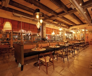 L’intérieur de ce restaurant se caractérise par de hauts plafonds, des poutres apparentes et une variété de types de sièges, notamment des banquettes et des tables.