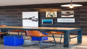 Un espace repas moderne avec une longue table en bois, des chaises en métal et des œuvres d’art accrochées au mur.
