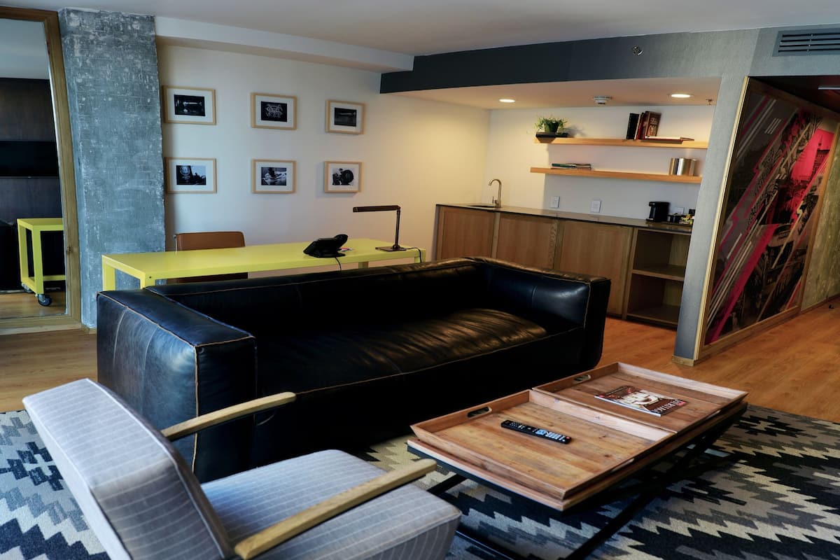 Un salon moderne avec un canapé en cuir noir, une table basse en bois et une table jaune. On y trouve également un coin cuisine avec des placards en bois et un évier.