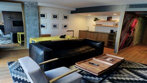 Un salon moderne avec un canapé en cuir noir, une table basse en bois et une table jaune. On y trouve également un coin cuisine avec des placards en bois et un évier.