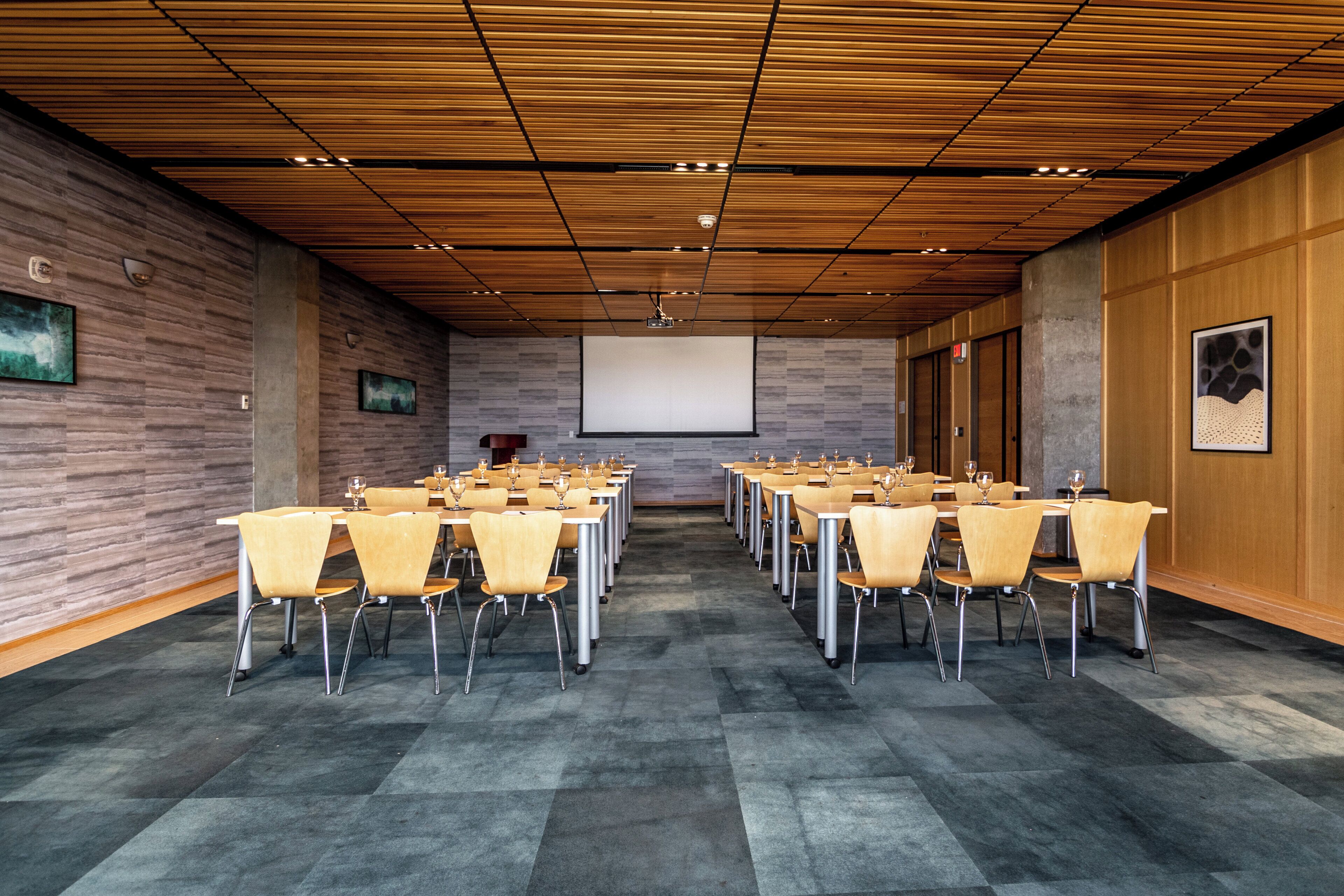 Un salón de conferencias con una mesa larga, sillas, una pantalla de proyector y un techo de madera.