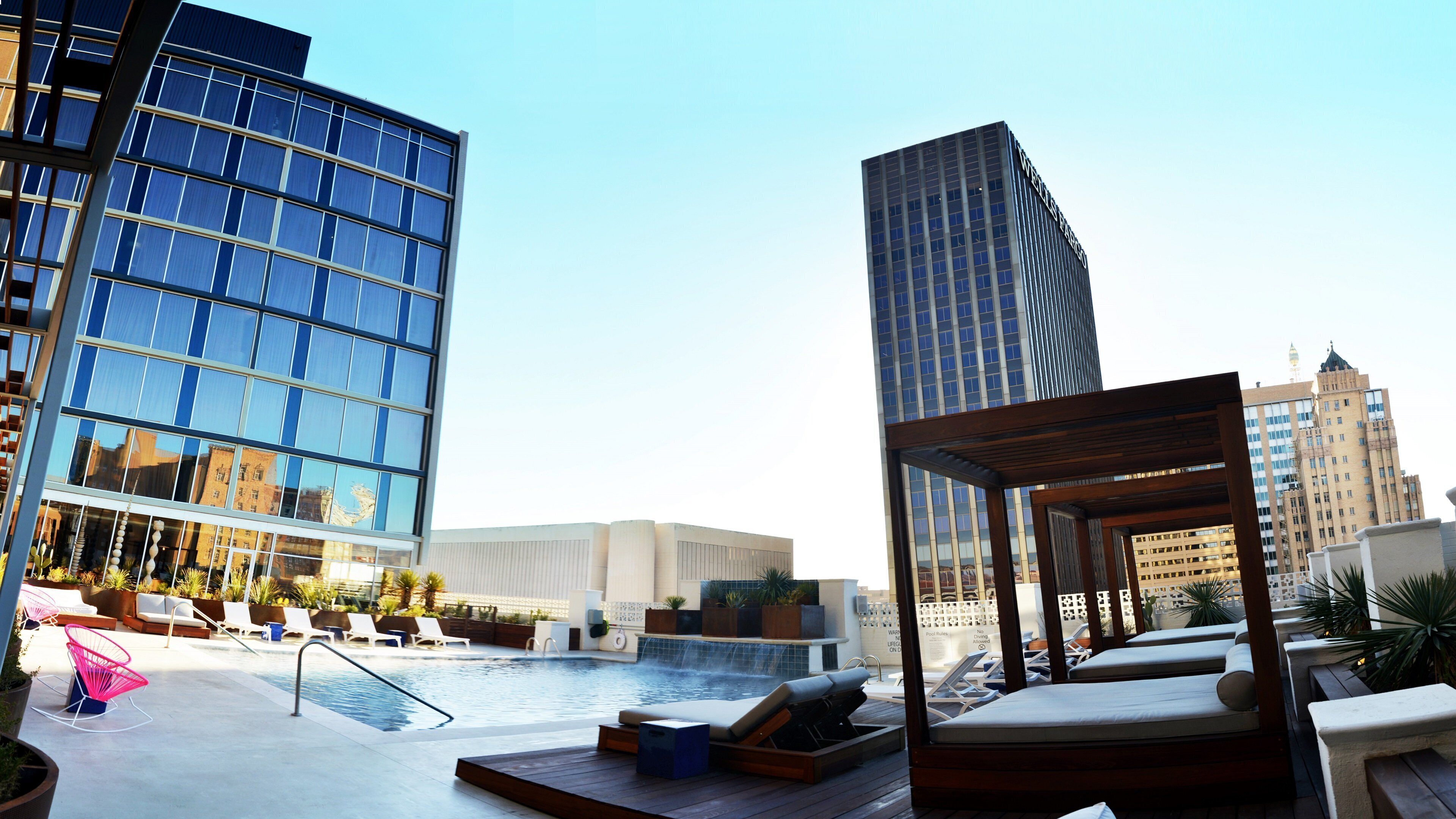 A rooftop pool area with lounge chairs and a view of modern buildings.