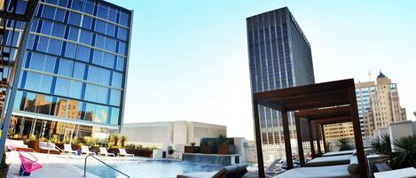 A rooftop pool area with lounge chairs and a view of modern buildings.