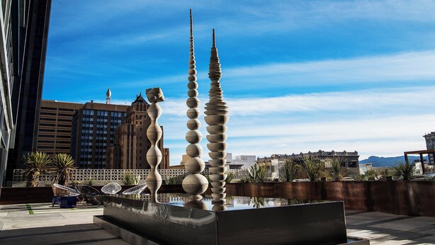 A modern sculpture with a reflective pool in an urban setting.