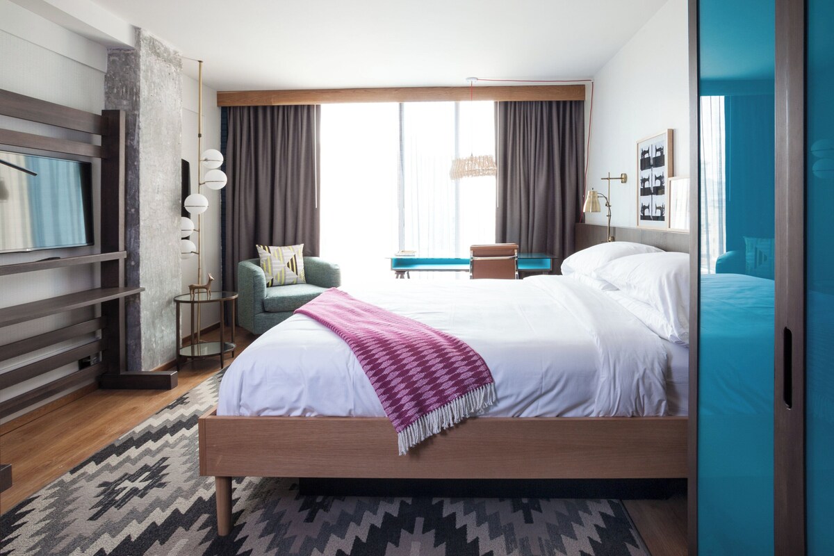 Une chambre d’hôtel moderne dotée d’un grand lit, d’un bureau, d’une chaise, d’une télévision et offrant une vue sur l’extérieur.