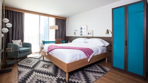 A modern hotel room with a large bed, a desk, a chair, and a wardrobe.