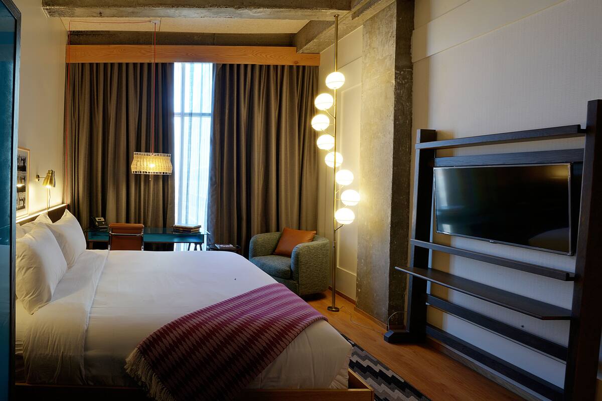 Une chambre d’hôtel avec un grand lit, un bureau avec une chaise, une télévision et une fenêtre avec des rideaux.