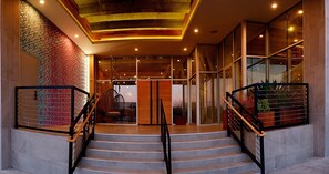 Un escalier menant à un hall d’entrée doté d’un mur orné de motifs, d’un plafond en bois et d’une porte d’entrée en verre.