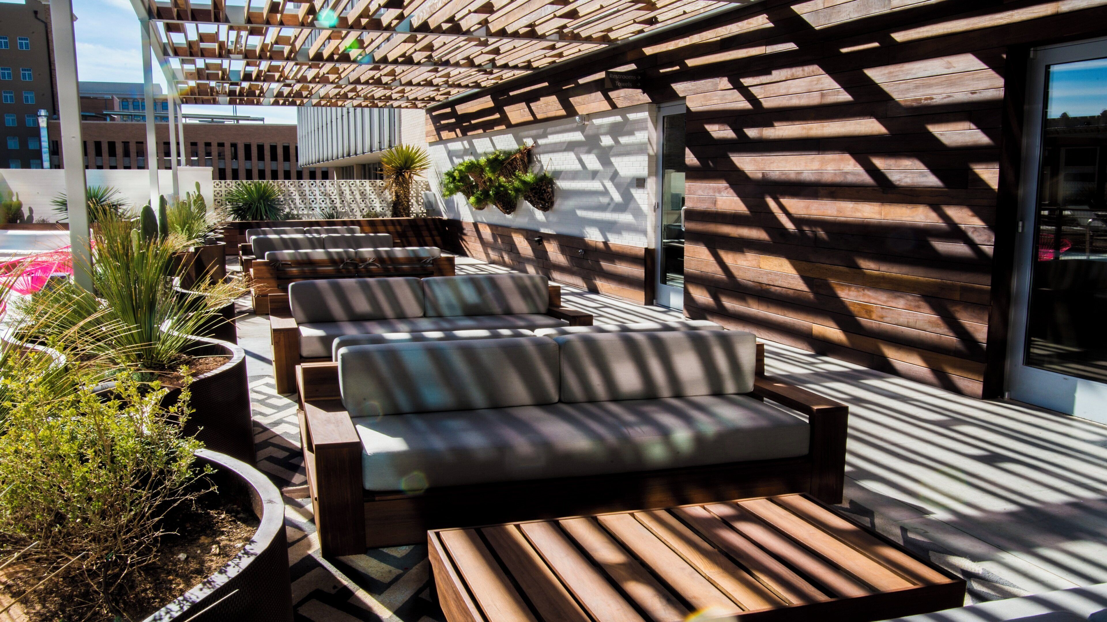 Un espacio de estar al aire libre con techo, bancos de madera y macetas.