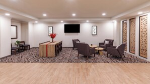 Una habitación amplia con piso de madera, una mesa central con sillas, un televisor montado en la pared y paneles decorativos en las paredes.