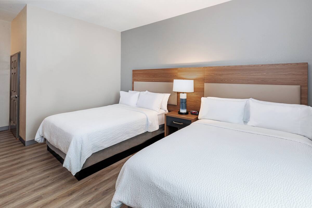 A hotel room with two beds, a wooden headboard, a nightstand with a lamp, and a door.