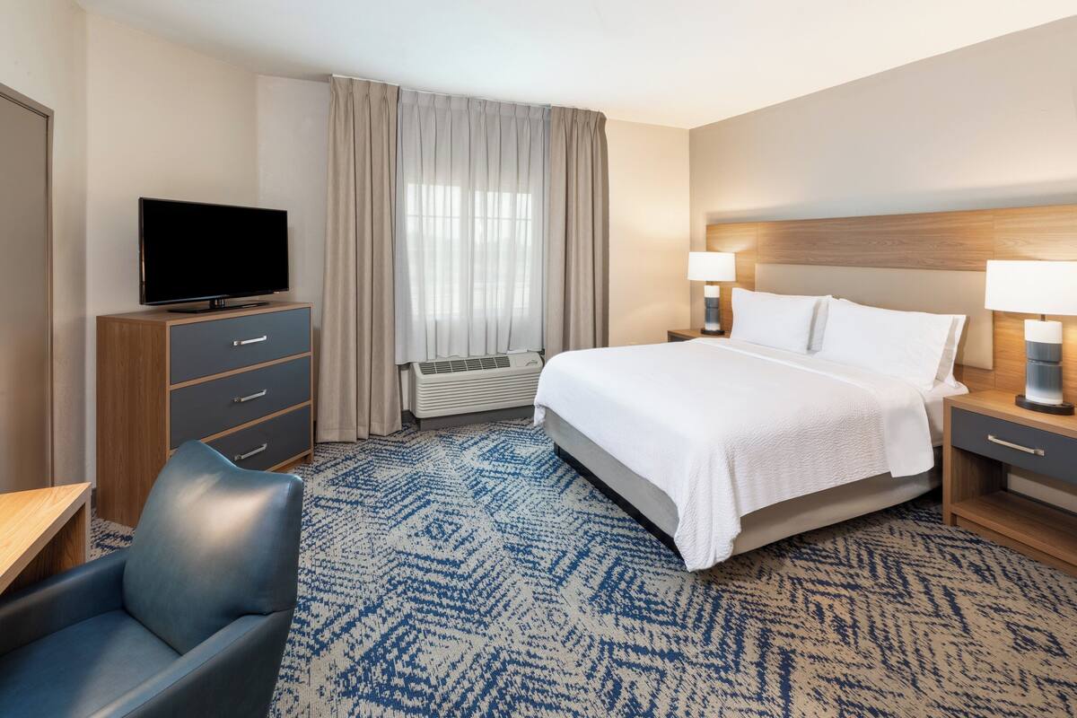 A hotel room with a bed, bedside lamps, a TV on a wooden cabinet, a desk, and a chair.