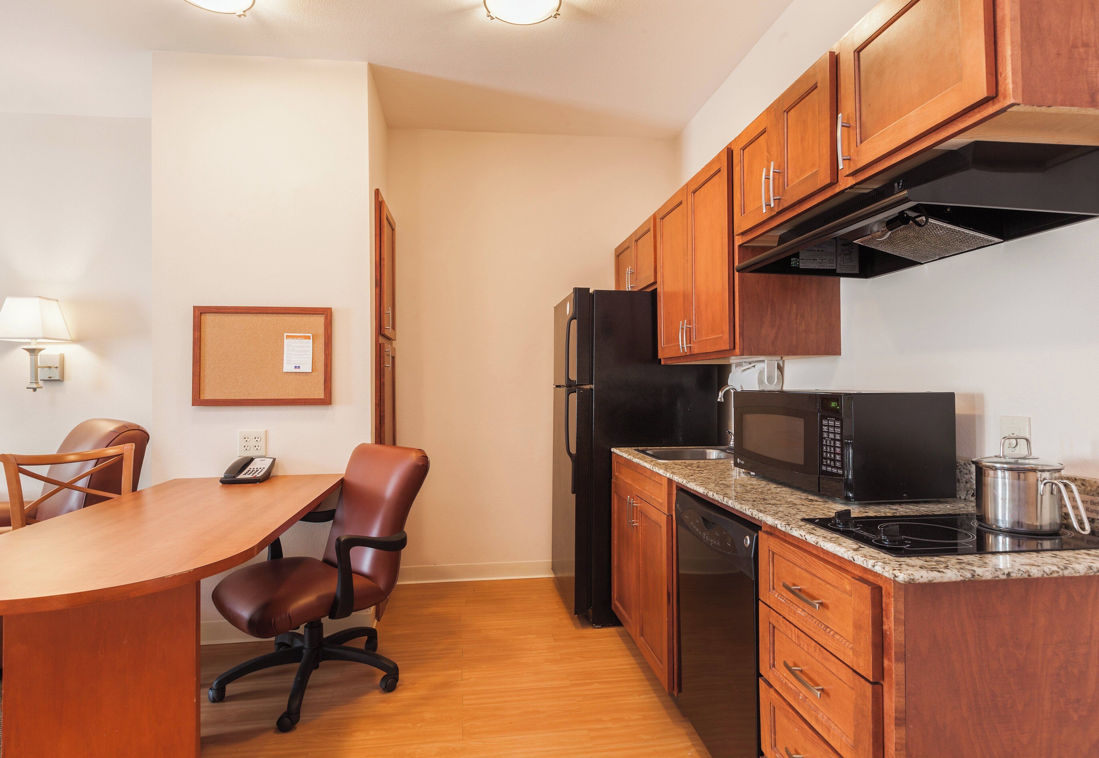 A compact kitchen with wooden cabinets, a refrigerator, a microwave, and a stove.