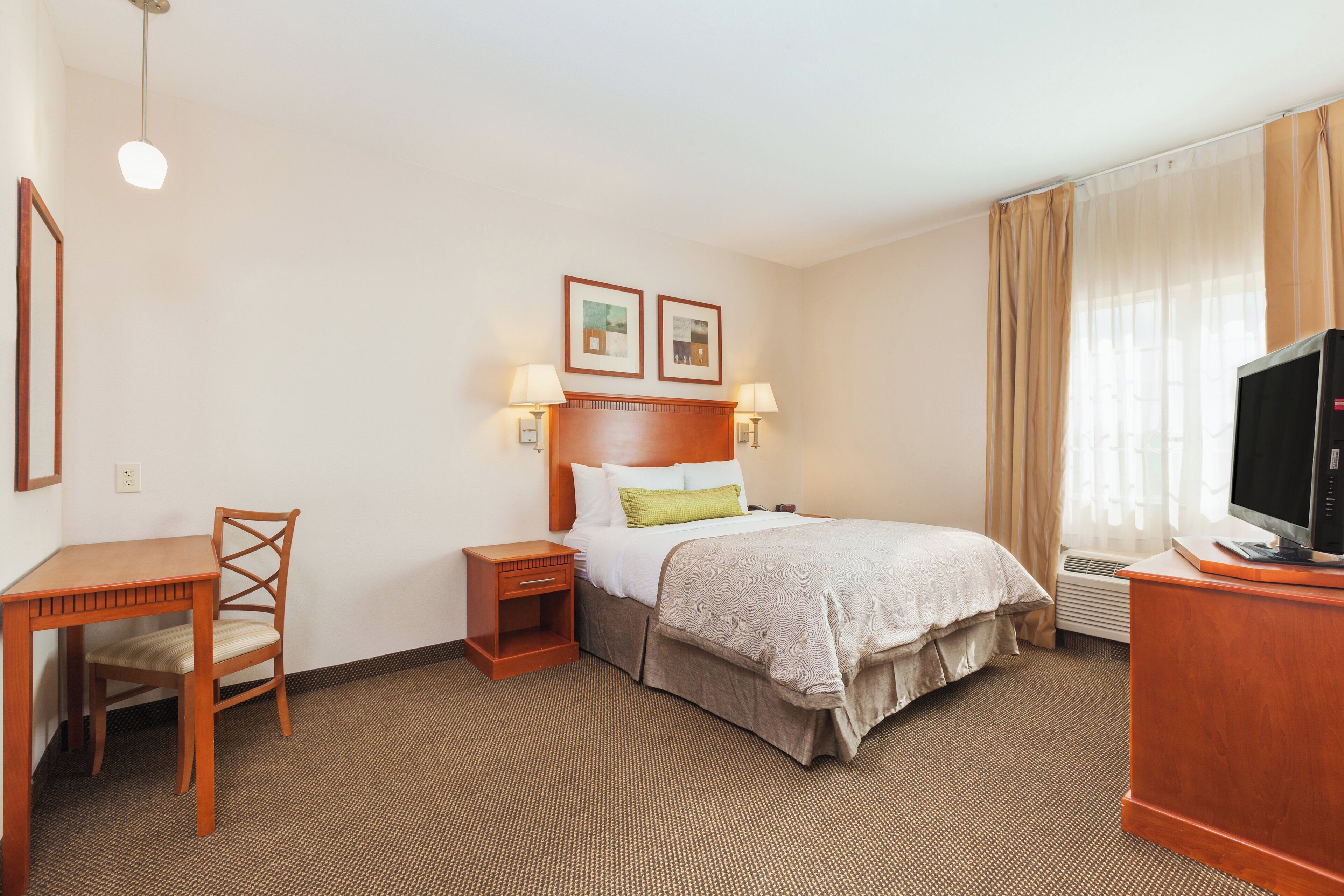 A hotel room with a bed, a desk, a chair, a television, and two wall-mounted lamps.